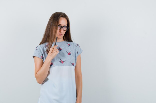 Tシャツのペンで顎に触れて物思いにふける若い女性。正面図。