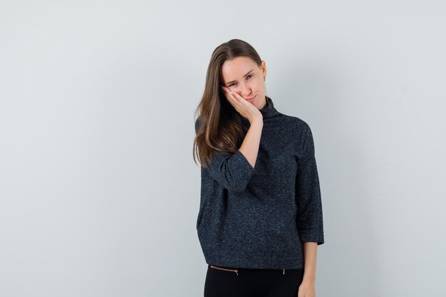 Young female touching her cheeks in black blouse and looking lovable. front view. space for text