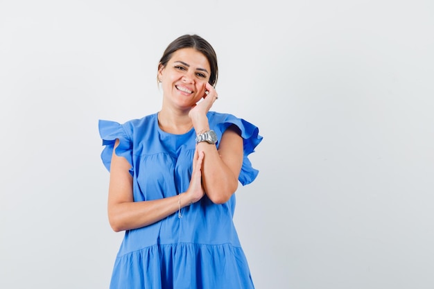 Free photo young female touching her face skin on cheek in blue dress and looking cheerful