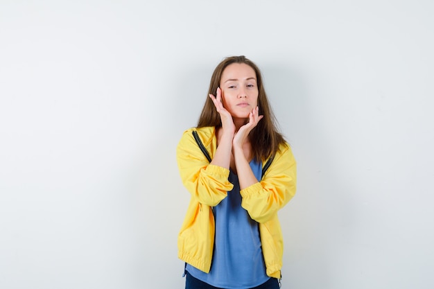 Young female touching her face skin in t-shirt, jacket and looking alluring, front view.