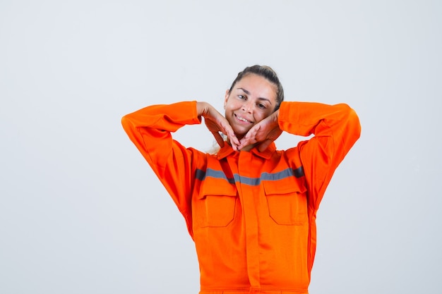 Young female touching her face with her hands in worker uniform and looking cute , front view.