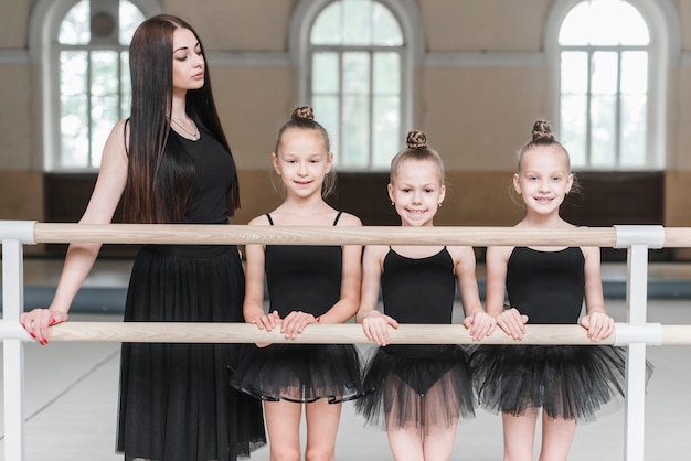 Young female trainer with her three ballerina girls standing behind the barre