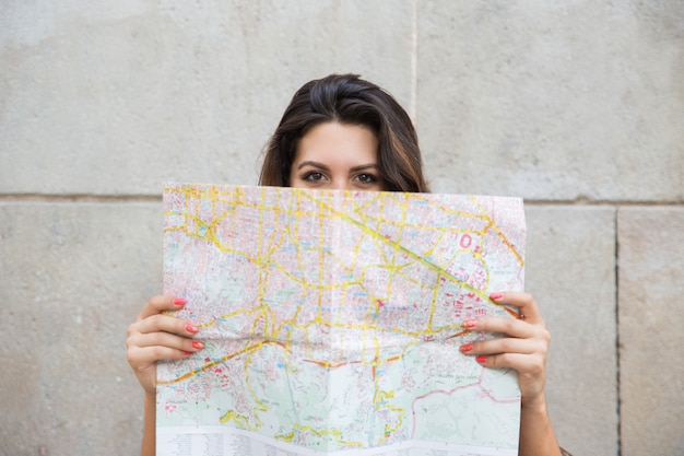 Free photo young female traveler peeking out from behind map