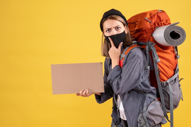 黒いマスクと段ボールを保持しているバックパックを持つ若い女性旅行者