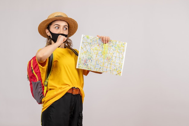 young female traveller with red backpack holding up map on grey