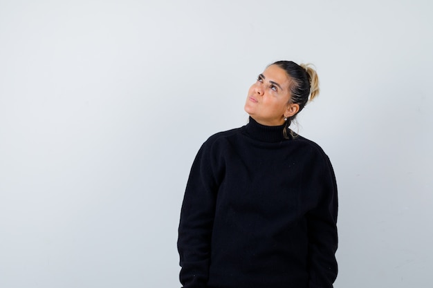 Young female in turtleneck sweater looking up and looking thoughtful , front view.