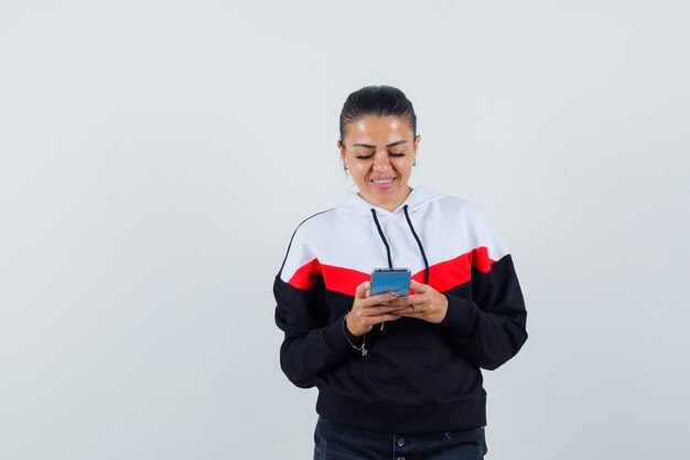 Young female typing message on phone in colorful sweatshirt and looking focused. front view.