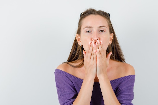 Young female in violet shirt holding hands on mouth , front view.