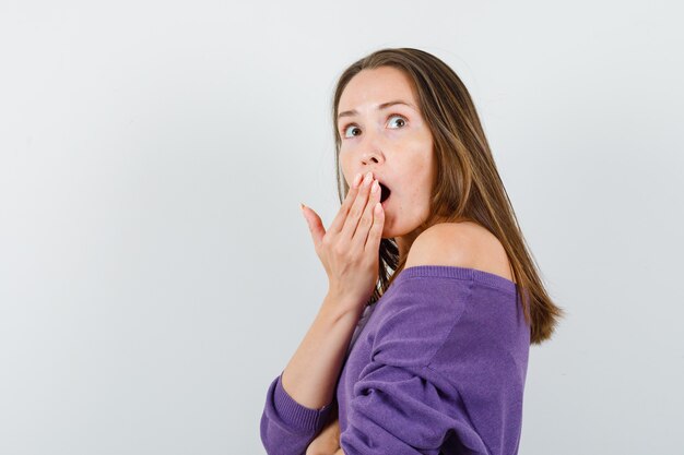 Young female in violet shirt looking up with hand over mouth and looking surprised .