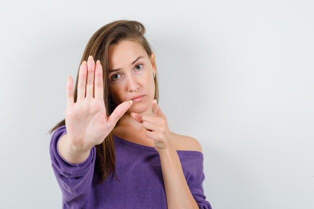 Young female in violet shirt pointing at camera with stop gesture and looking serious , front view.