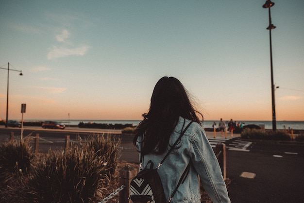 Young female walking on the sidewalk with a back and clear blue sky