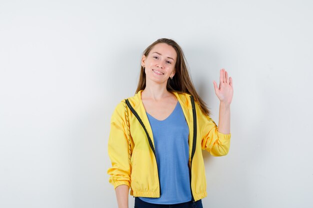 Young female waving hand to say goodbye in t-shirt and looking jolly. front view.