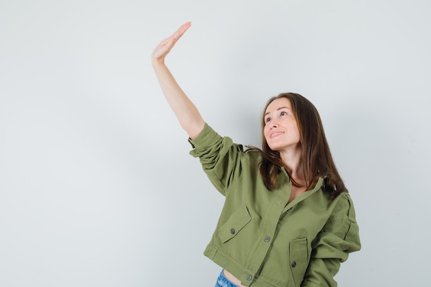 Young female waving hand while looking up in jacket, front view.