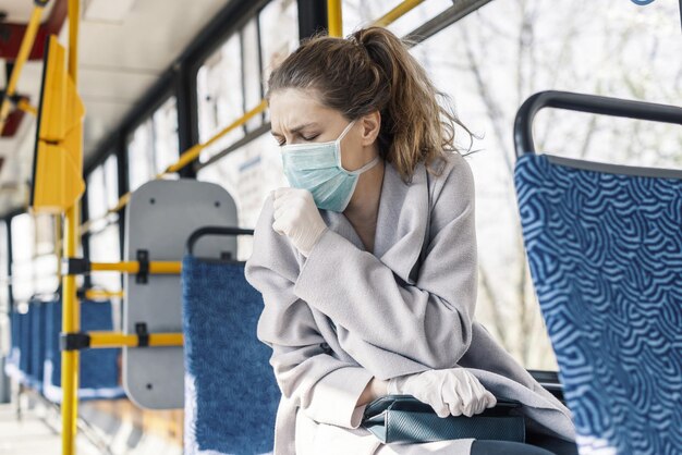 フェイスマスクを着用し、ライトの下の公共交通機関で咳をする若い女性 - COVID-19