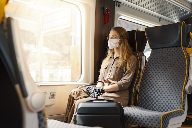 Young female wearing a facemask and sitting in a train under the sunlight