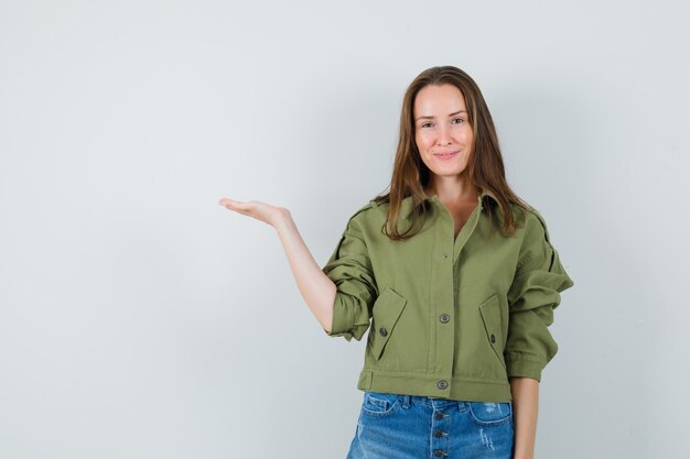 Young female welcoming or showing something in jacket, shorts and looking confident , front view.