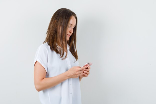 Young female in white blouse looking at phone and looking focused