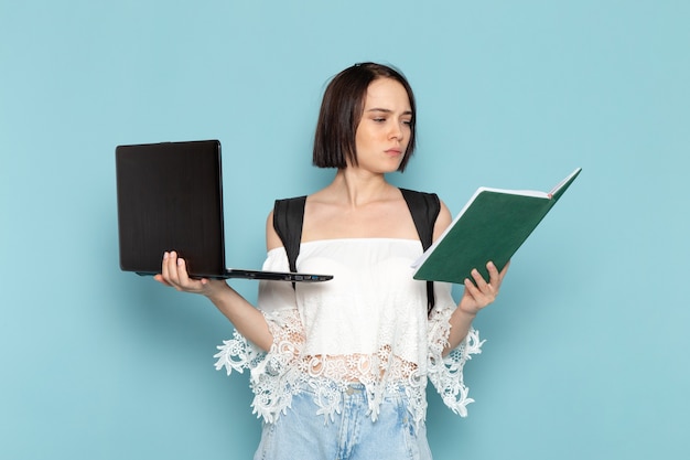 young female in white shirt and black bag holding copybook with laptop on blue