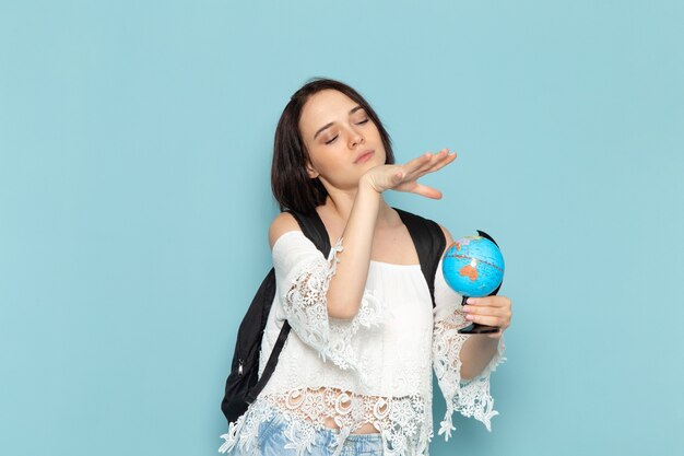 young female in white shirt and black bag holding globe on blue