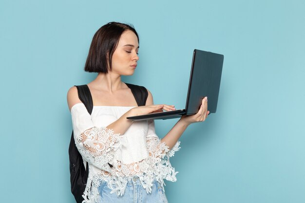 young female in white shirt and black bag using laptop on blue