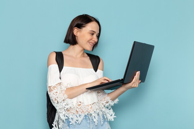 young female in white shirt and black bag using laptop with smile on blue