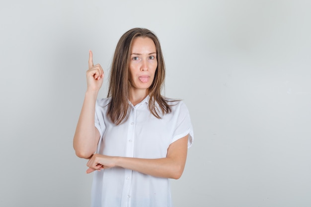 Giovane donna in camicia bianca, che mostra la lingua con il dito in alto