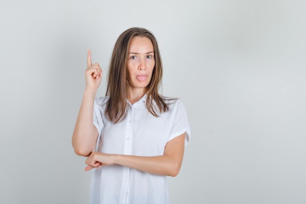 Молодая женщина в белой рубашке, показывая язык с пальцем вверх