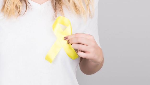 Young female in white t-shirt holding yellow ribbon awareness symbol for suicide, sarcoma bone cancer, bladder cancer, liver cancer and childhood cancer concept. health care.