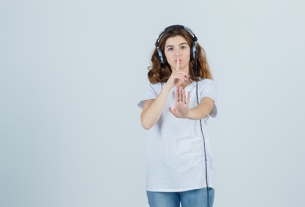 Young female in white t-shirt showing silence gesture with silence sign and looking careful , front view.