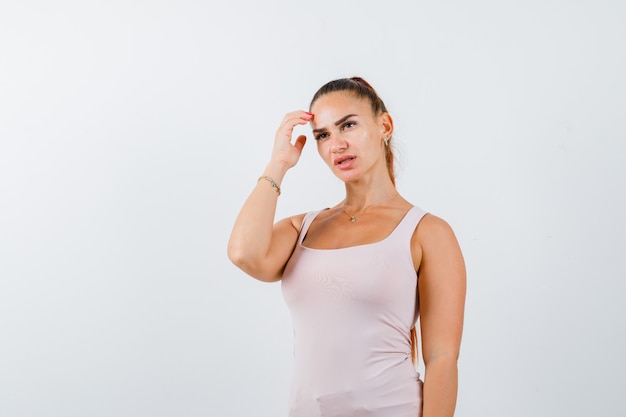 Young female in white tank top scratching head and looking thoughtful , front view.