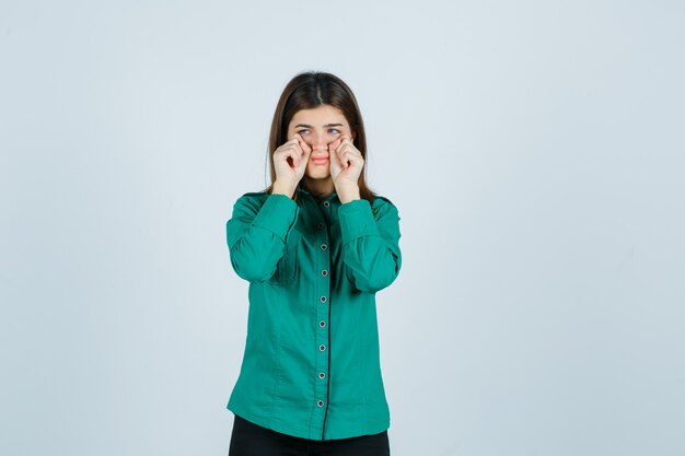 Young female wiping tears with hands in green shirt and looking offended. front view.