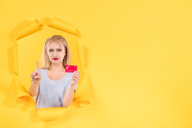破れた黄色い紙の表面の貯金箱の買い物でクレジットカードを持つ若い女性