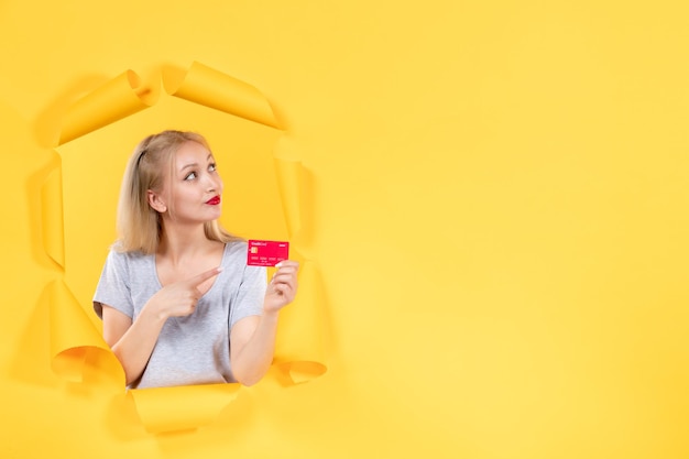 Young female with credit card on torn yellow paper background bank sale shopping