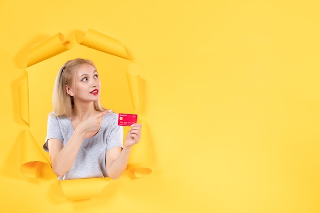 引き裂かれた黄色い紙の背景にクレジットカードを持つ若い女性貯金箱販売ショッピング
