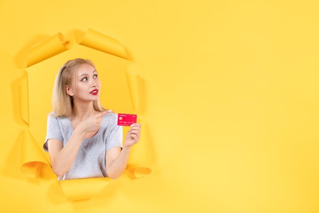 Young female with credit card on torn yellow paper background money bank sale shopping