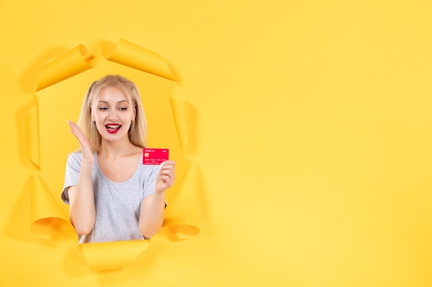 引き裂かれた黄色い紙の背景の貯金箱の買い物でクレジットカードを持つ若い女性
