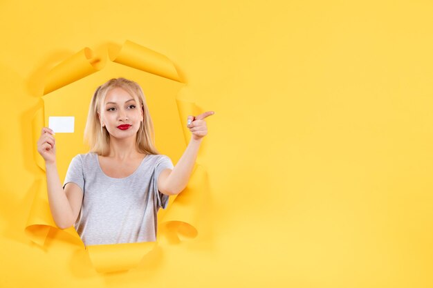 Young female with credit card on the yellow wall