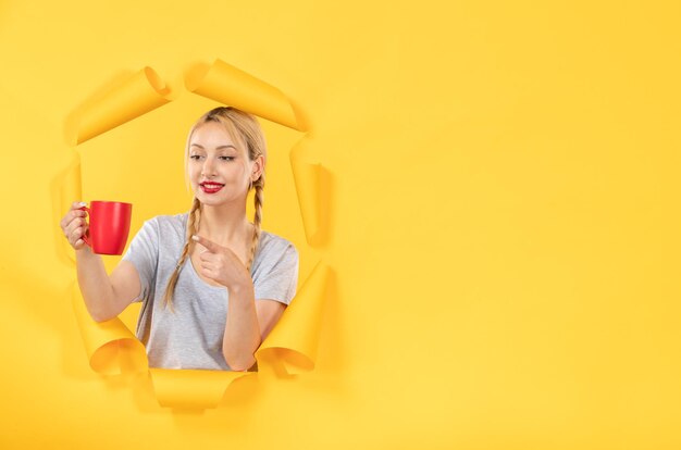 Young female with cup of tea on yellow paper background shopping advertising facials