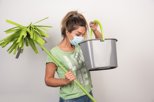 Free photo young female with facemask looking at mop on white wall.