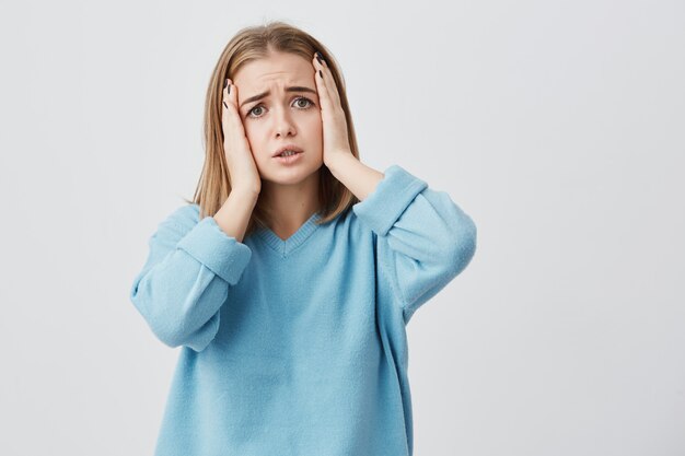 Young female with fair hair having discontent look plugging her ears being annoyed with noise wanting silence and calm atmosphere being exhausted of loud sound and noise.