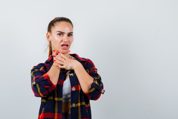 Young female with hands on throat in crop top, checkered shirt and looking unwell , front view.