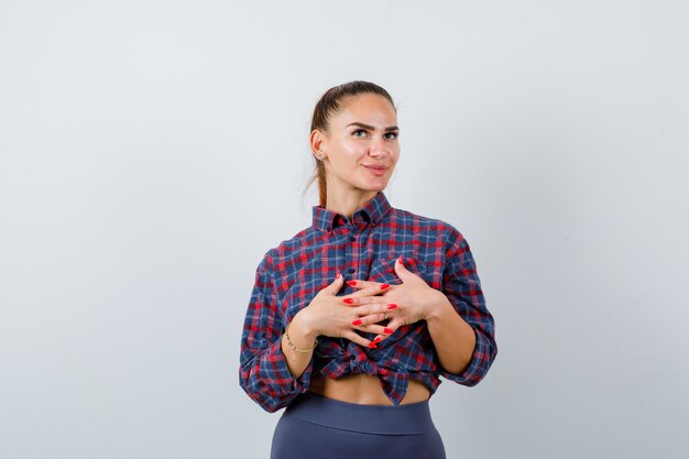 Young female with hands with intertwined fingers in front of her in checkered shirt, pants and looking pensive. front view.