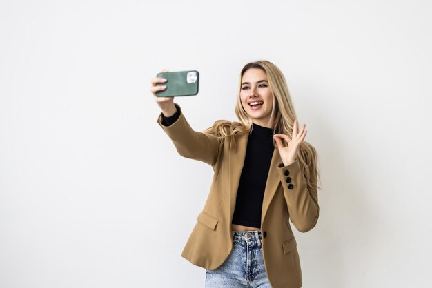 Young female with long blonde holding mobile phone posing for selfie looking at camera with flirty smile Attractive woman making video call