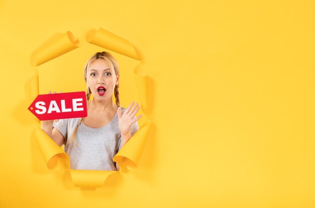 Young female with sale inscription sign on a torn yellow paper background shopping indoor facial