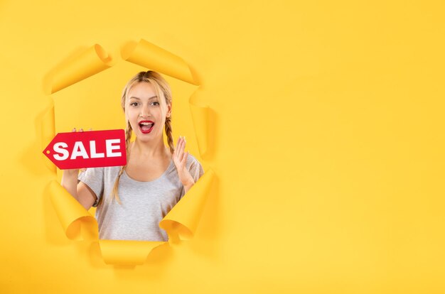 Young female with sale inscription sign on torn yellow paper background shopping indoor facials