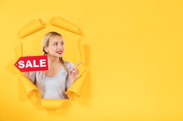 Young female with sale inscription sign on a torn yellow paper surface