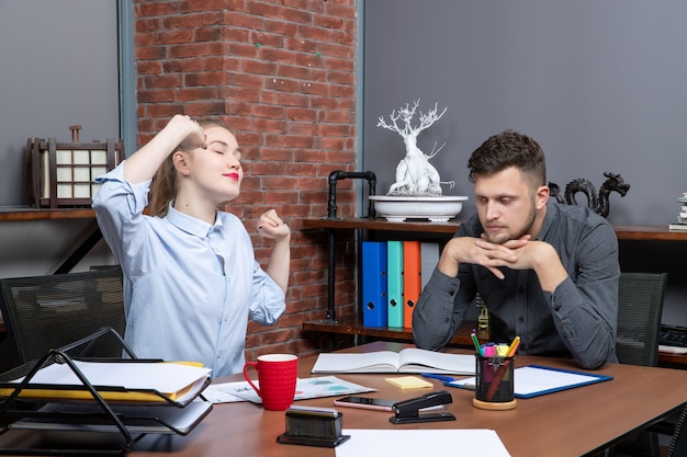 Foto gratuita giovane lavoratrice e il suo collega di lavoro seduti stanchi al tavolo in ufficio