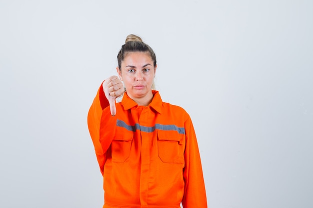 Foto gratuita giovane donna in uniforme da lavoro che mostra il pollice verso il basso e sembra scontenta, vista frontale.