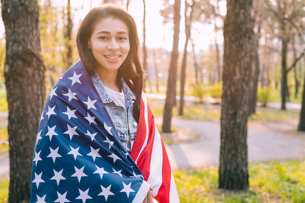 自然の中でアメリカの国旗を包む若い女性