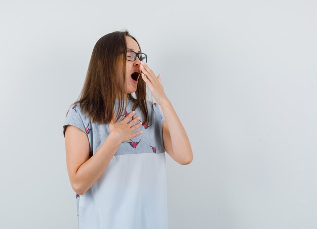 Tシャツであくびをして眠そうな若い女性。正面図。